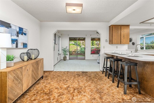 kitchen with light carpet, a textured ceiling, brown cabinetry, a breakfast bar area, and light countertops