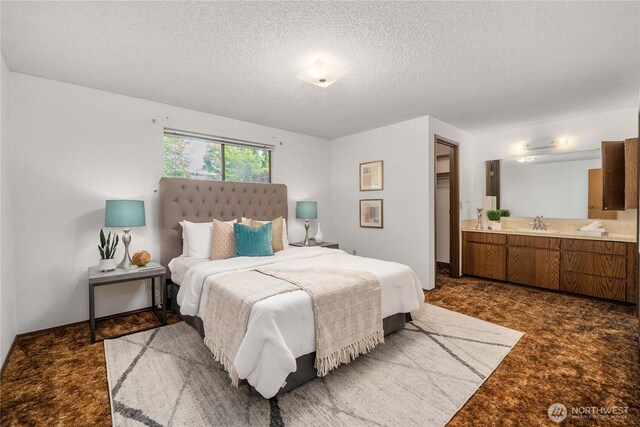 bedroom featuring a textured ceiling, connected bathroom, dark colored carpet, and a sink