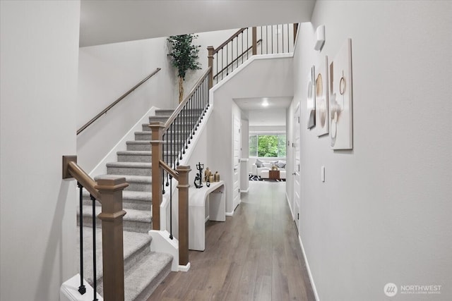 stairs featuring baseboards, wood finished floors, and a high ceiling