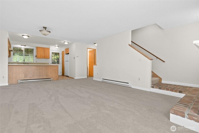 unfurnished living room with baseboard heating, light colored carpet, baseboards, and stairway