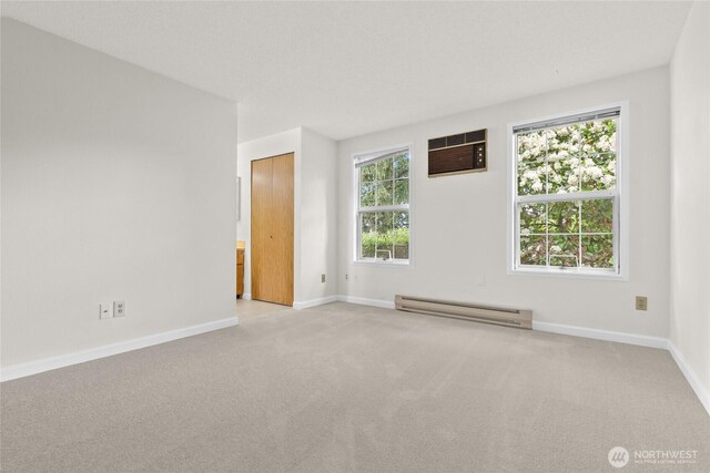 unfurnished room featuring a baseboard radiator, an AC wall unit, baseboards, and carpet flooring