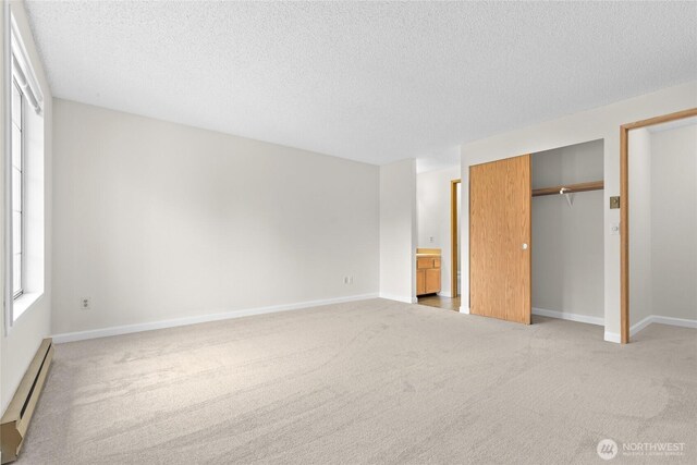 unfurnished bedroom featuring a baseboard heating unit, a textured ceiling, light colored carpet, a closet, and baseboards