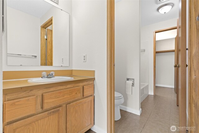 bathroom featuring toilet, tile patterned flooring, vanity, baseboards, and a bathtub