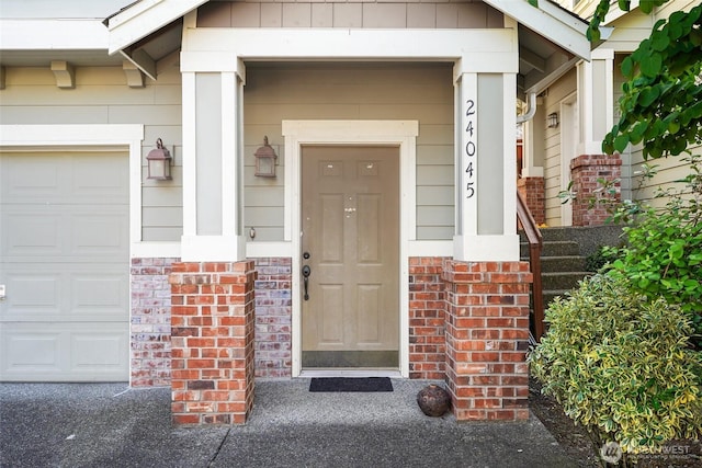 doorway to property with brick siding, an attached garage, and covered porch