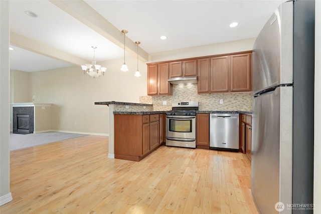 kitchen featuring appliances with stainless steel finishes, a peninsula, under cabinet range hood, light wood-type flooring, and brown cabinetry