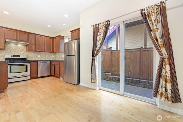 kitchen with stainless steel appliances, light wood finished floors, under cabinet range hood, decorative backsplash, and brown cabinets