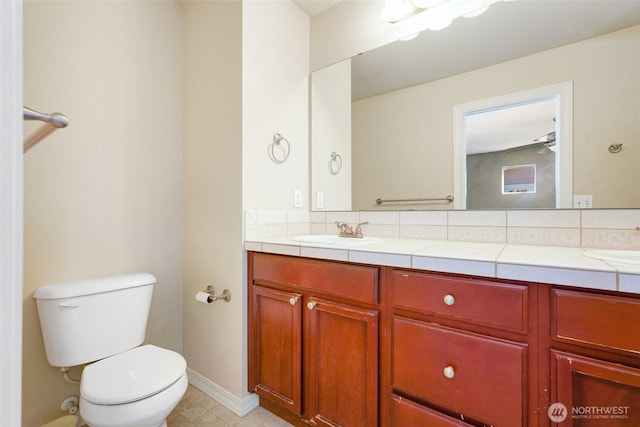 bathroom with toilet, double vanity, backsplash, and baseboards