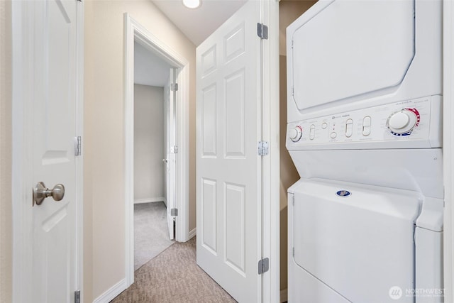 laundry area with stacked washing machine and dryer, light carpet, and baseboards