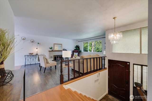 foyer featuring wood finished floors, a chandelier, a brick fireplace, and baseboards