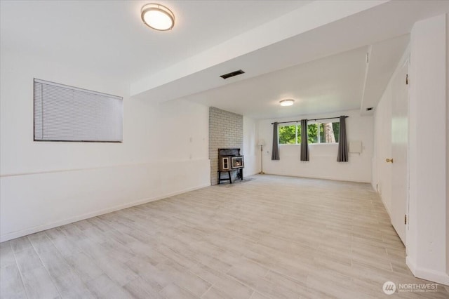 unfurnished living room featuring a wood stove, light wood-style floors, and baseboards