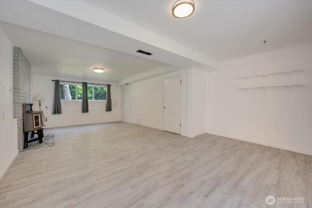 unfurnished living room with a wood stove, light wood-type flooring, and baseboards