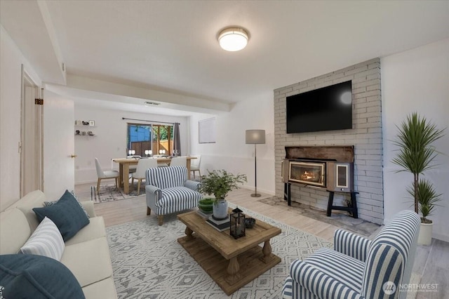 living area featuring light wood finished floors, a brick fireplace, and baseboards