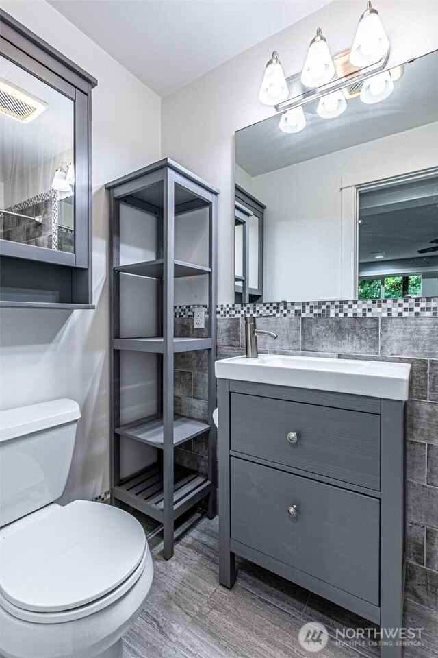 bathroom with tile walls, toilet, wood finished floors, and vanity