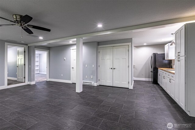 basement featuring a baseboard radiator, a ceiling fan, baseboards, recessed lighting, and freestanding refrigerator
