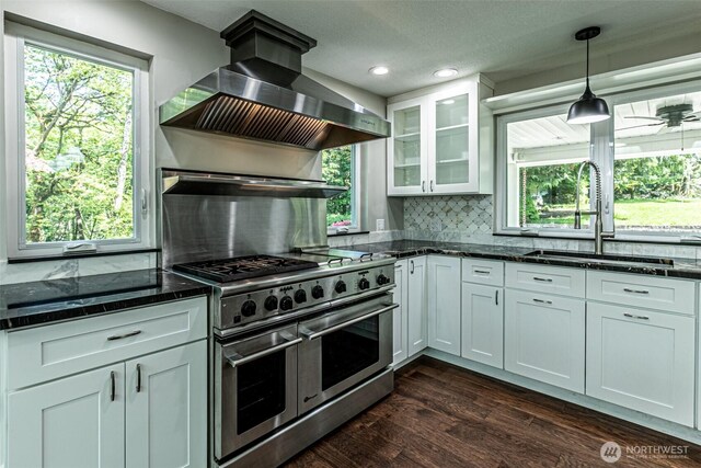 kitchen featuring range hood, a sink, double oven range, backsplash, and glass insert cabinets