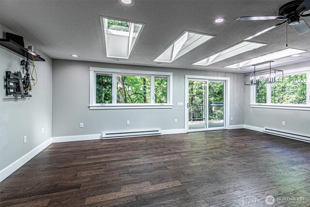 unfurnished room with a baseboard heating unit, a skylight, baseboards, a textured ceiling, and wood finished floors