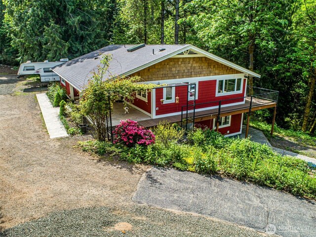 view of front of home with driveway, a view of trees, and a wooden deck