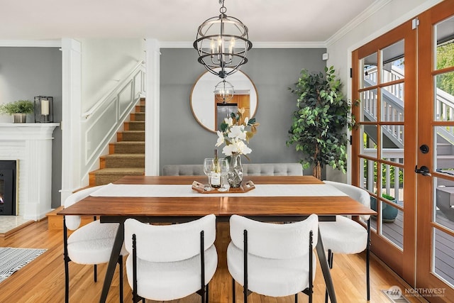 dining space featuring wood finished floors, stairway, crown molding, a fireplace, and a chandelier