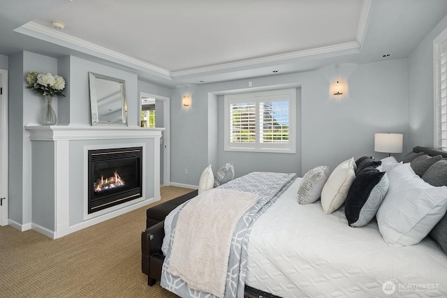 carpeted bedroom with a tray ceiling, crown molding, a glass covered fireplace, and baseboards