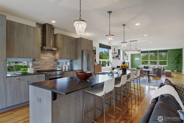 kitchen with wall chimney range hood, a sink, open floor plan, high end appliances, and healthy amount of natural light