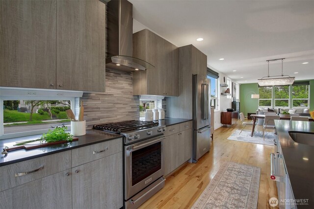 kitchen with premium appliances, wall chimney exhaust hood, dark countertops, modern cabinets, and recessed lighting