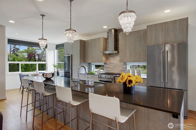 kitchen with premium appliances, wall chimney range hood, a chandelier, a sink, and backsplash