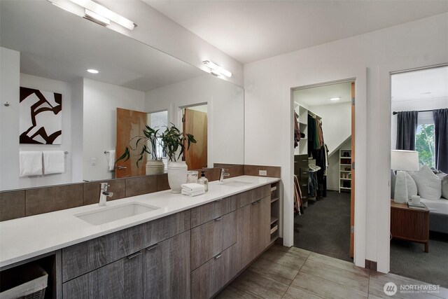 ensuite bathroom with double vanity, a walk in closet, and recessed lighting