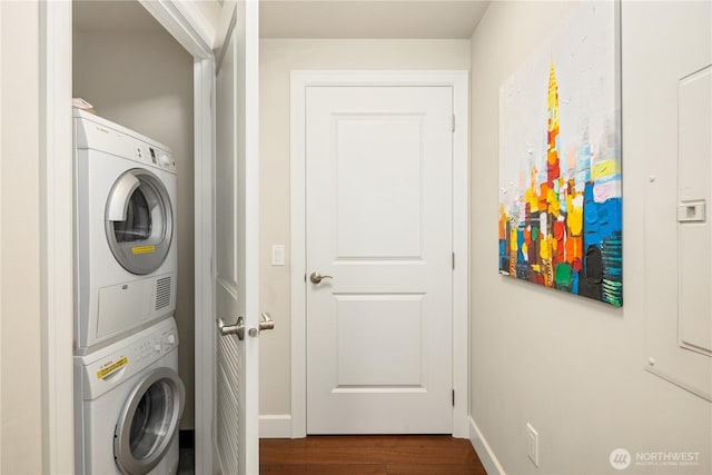 laundry area featuring stacked washer / dryer, dark wood-style flooring, and baseboards