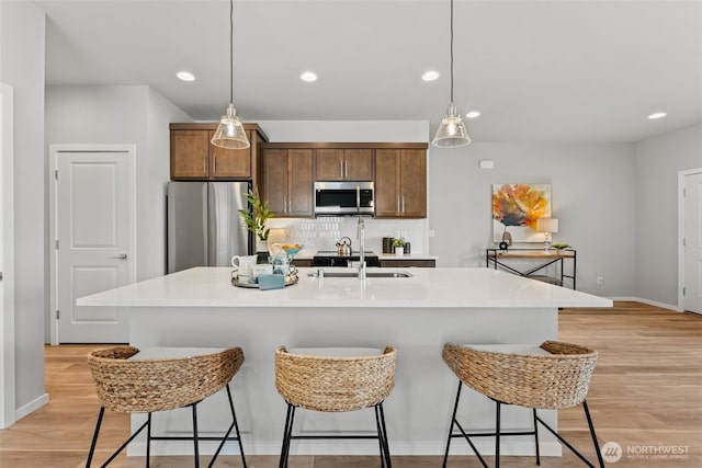 81 E Compass Ln, Allyn, WA 98524 - kitchen featuring appliances with stainless steel finishes, a sink, light wood-style floors, decorative backsplash, and decorative light fixtures