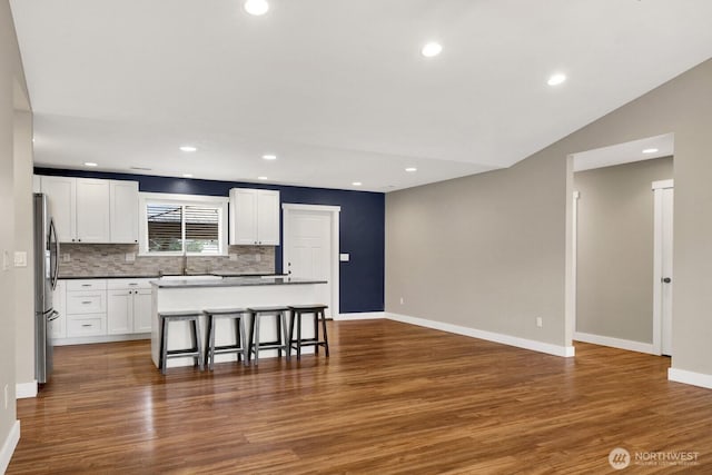 kitchen with freestanding refrigerator, a breakfast bar, dark wood-style floors, recessed lighting, and vaulted ceiling