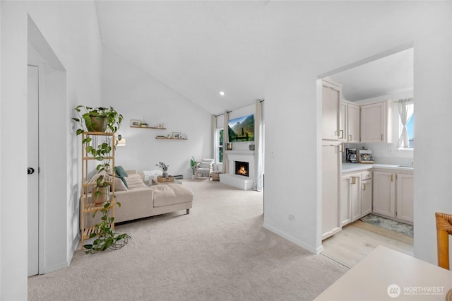living room featuring light colored carpet, vaulted ceiling, and a warm lit fireplace