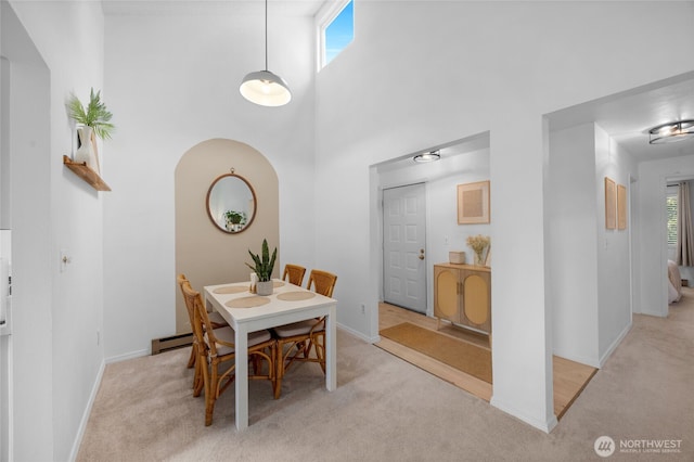 dining space featuring light colored carpet, baseboards, a baseboard radiator, and a towering ceiling