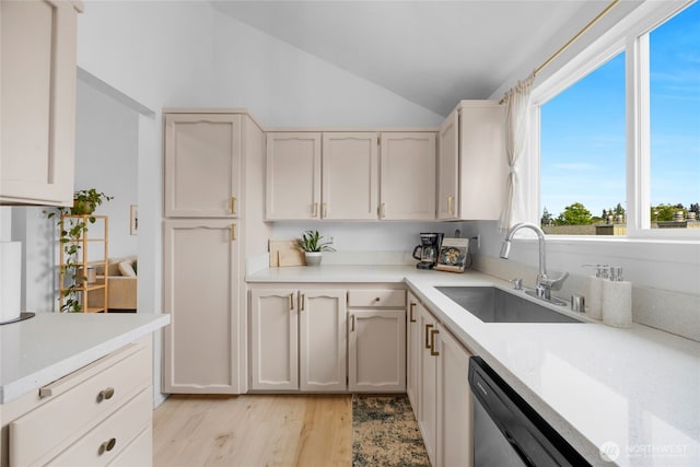 kitchen featuring dishwashing machine, a sink, vaulted ceiling, light wood-style floors, and light countertops