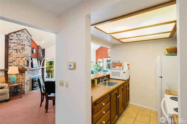 kitchen with white appliances, a sink, vaulted ceiling, a fireplace, and baseboards