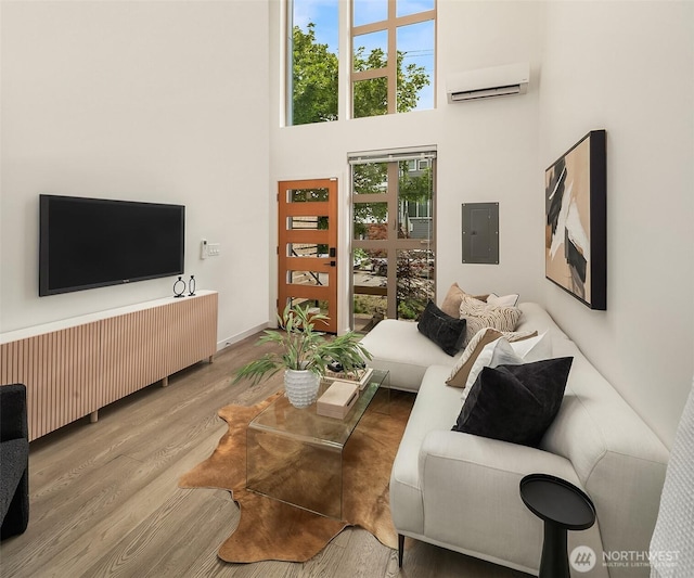 living room featuring an AC wall unit, electric panel, wood finished floors, a towering ceiling, and baseboards