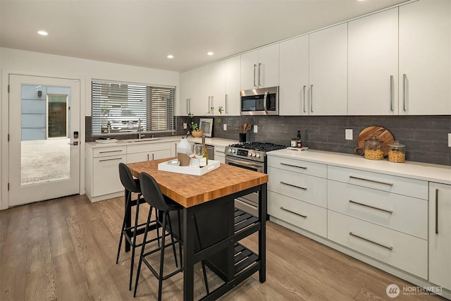 kitchen with appliances with stainless steel finishes, a sink, light wood-type flooring, tasteful backsplash, and white cabinets