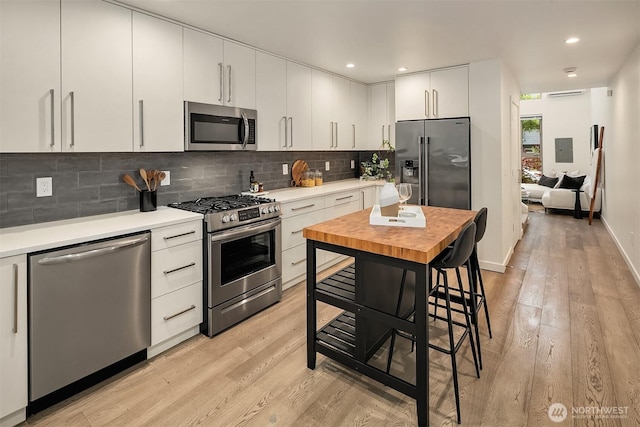 kitchen featuring stainless steel appliances, light wood-type flooring, backsplash, white cabinets, and recessed lighting