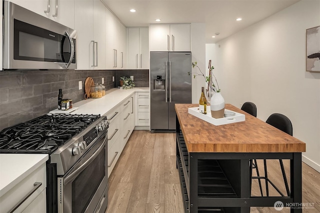 kitchen with stainless steel appliances, wooden counters, light wood-type flooring, decorative backsplash, and white cabinetry