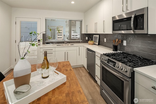 kitchen featuring stainless steel appliances, a sink, light countertops, decorative backsplash, and white cabinetry