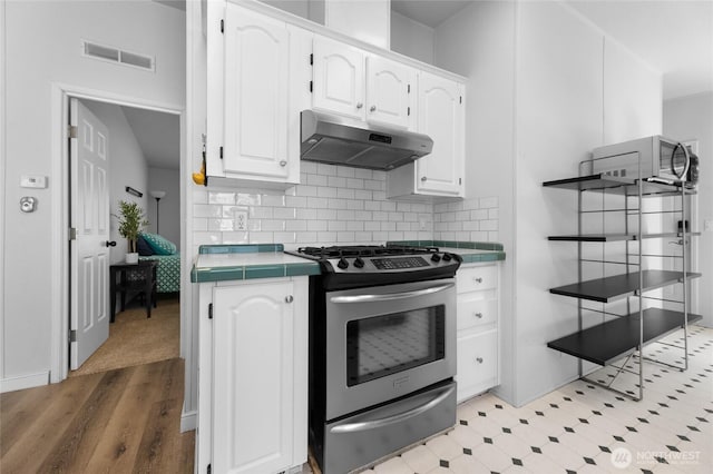 16037 Vail Loop Rd SE, Rainier, WA 98576 - kitchen featuring under cabinet range hood, stainless steel gas range oven, tile countertops, white cabinetry, and backsplash