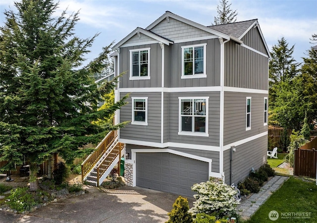 view of front of house with board and batten siding, driveway, a garage, stairs, and fence