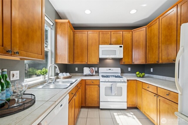 kitchen featuring white appliances, a sink, light tile patterned floors, recessed lighting, and brown cabinets