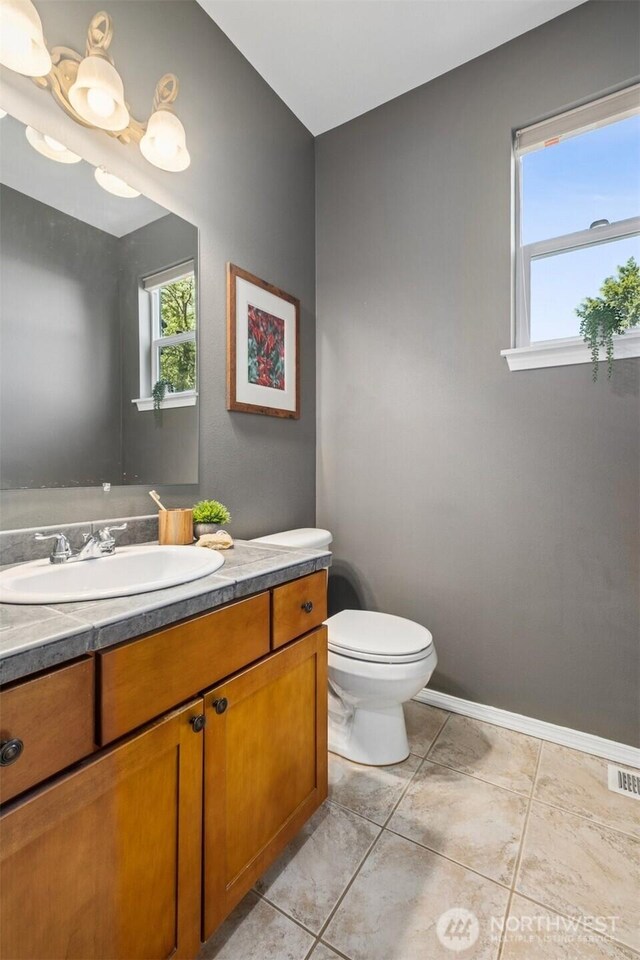 half bathroom featuring toilet, tile patterned floors, vanity, and baseboards