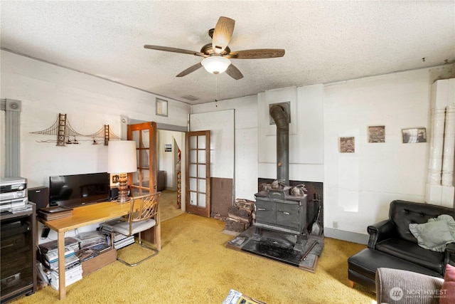 carpeted office space featuring a ceiling fan, a wood stove, and a textured ceiling