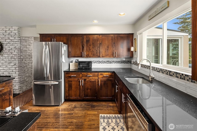 kitchen with stainless steel appliances, a sink, dark stone counters, dark wood-style flooring, and decorative backsplash