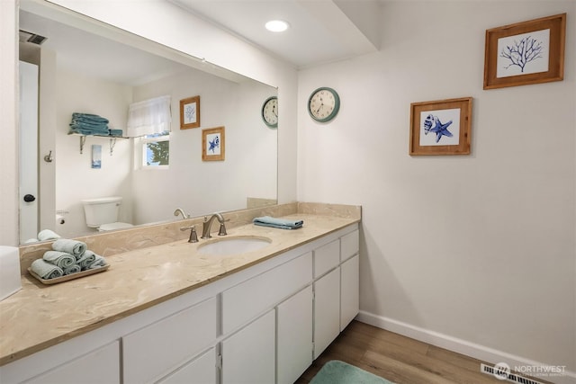 half bath featuring wood finished floors, baseboards, vanity, and toilet