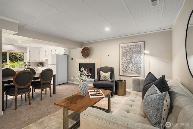 living area with light colored carpet, a drop ceiling, a tiled fireplace, recessed lighting, and baseboards