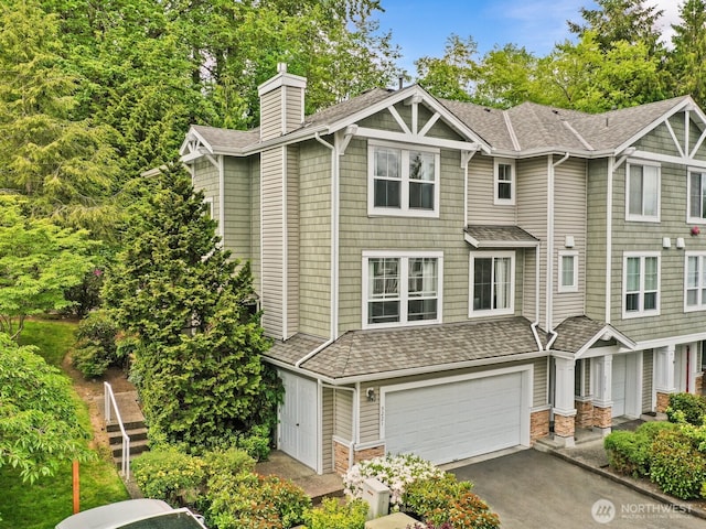 view of property with a shingled roof, an attached garage, a chimney, and driveway