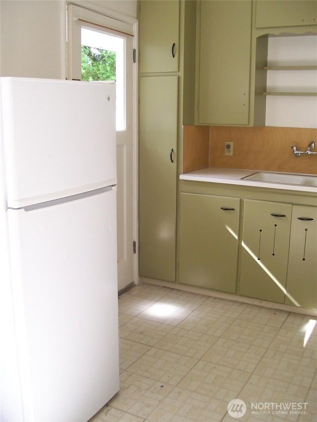 kitchen featuring freestanding refrigerator, a sink, light countertops, light flooring, and tasteful backsplash