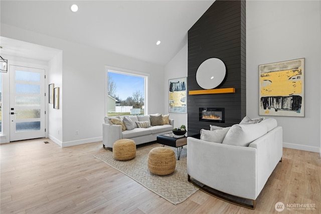 living area featuring high vaulted ceiling, baseboards, plenty of natural light, a fireplace, and light wood-style floors